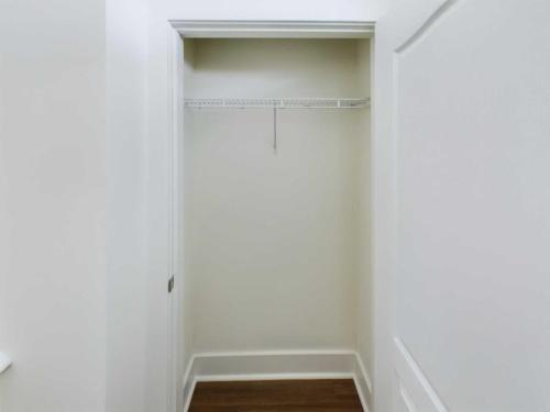 Apartments in Lebanon, IN A small, empty closet with white walls, a single white wire shelf, and open double doors facing hardwood flooring.