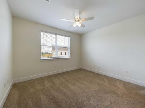 Apartments in Lebanon, IN A clean, empty room with beige carpet, white walls, a ceiling fan with light, and a window with blinds allowing natural light in.