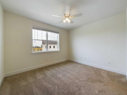 Apartments in Lebanon, IN Empty room with beige carpet, a white ceiling fan, and a large window with a view of neighboring buildings. The walls are painted white.