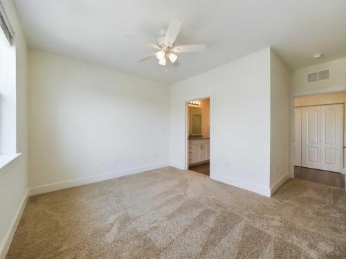 Apartments in Lebanon, IN A spacious empty bedroom with beige carpet, a ceiling fan, and white walls. An open door leads to a bathroom with a sink and mirror. Another door leads to what appears to be a closet.