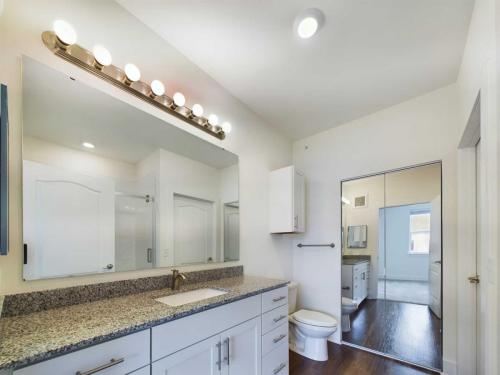 Apartments in Lebanon, IN A modern bathroom with a granite countertop, large mirror with vanity lights, toilet, and shower. The floor is wooden, and there is a mirrored closet door in the background.