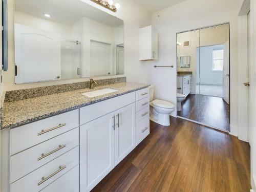 Apartments in Lebanon, IN A bathroom with a granite countertop, white cabinets, a large mirror, a toilet, and wooden flooring. There is a glass-door shower and a mirrored closet door reflecting more of the room.