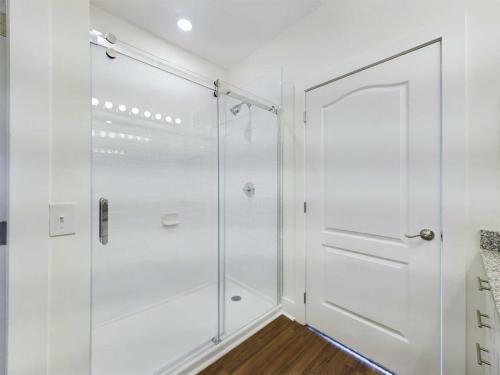 Apartments in Lebanon, IN Modern bathroom with a glass-enclosed shower, white tiled walls, wooden floor, and a white door with a handle.