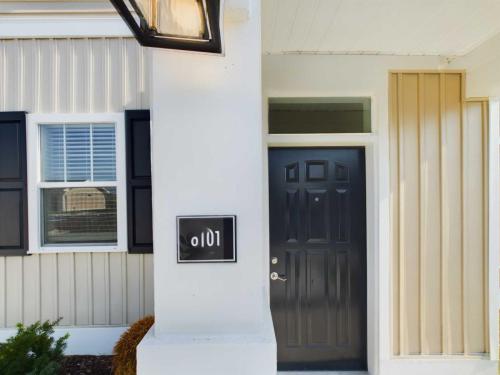 Apartments in Lebanon, IN A close-up of a residential entrance with a black door, adjacent window with closed shutters, and a small sign labeled 101 mounted on the white wall next to the door.