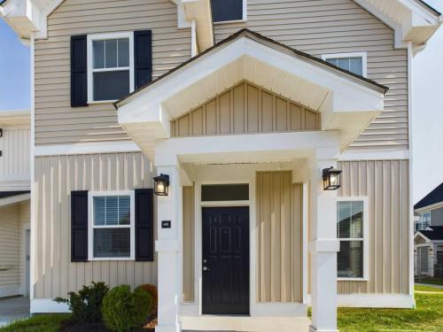 Apartments in Lebanon, IN The front view of a two-story beige house with white trim, black shutters, and a black door with sidelights. The entrance has a small porch with two lamps, situated among green landscaping.