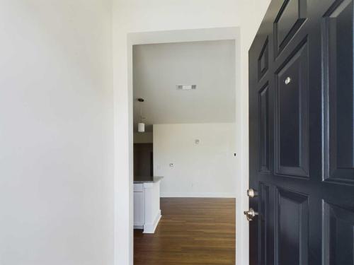 Apartments in Lebanon, IN View of an apartment entryway with a black door, hardwood floors, and an open layout leading to a kitchen area with white cabinets under pendant lights.