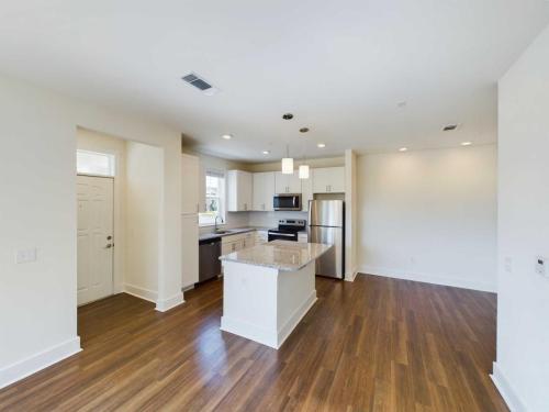 Apartments in Lebanon, IN Modern kitchen with an island, stainless steel appliances, white cabinets, light granite countertops, recessed lighting, and hardwood floors.