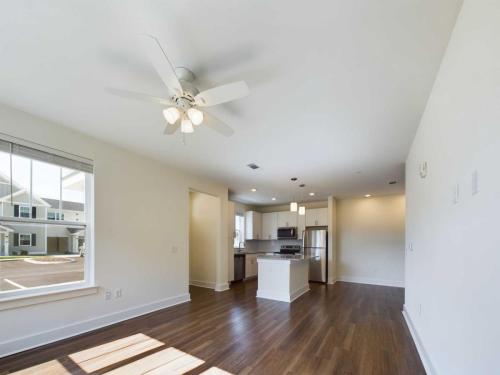 Apartments in Lebanon, IN A spacious, unfurnished living room with a ceiling fan, adjacent to an open-concept kitchen featuring modern appliances and hardwood flooring. Large window allows natural light to enter.