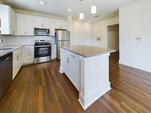 Apartments in Lebanon, IN A modern kitchen with wooden floors, white cabinets, stainless steel appliances, and a central island with granite countertops. Three pendant lights hang above the island.