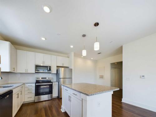 Apartments in Lebanon, IN A modern kitchen featuring white cabinetry, stainless steel appliances, a center island with granite countertops, two pendant lights, and wooden flooring.