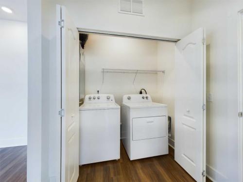 Apartments in Lebanon, IN A laundry area with a washing machine and dryer inside an open closet with white doors and a wooden floor. A wire shelf is installed above the machines.