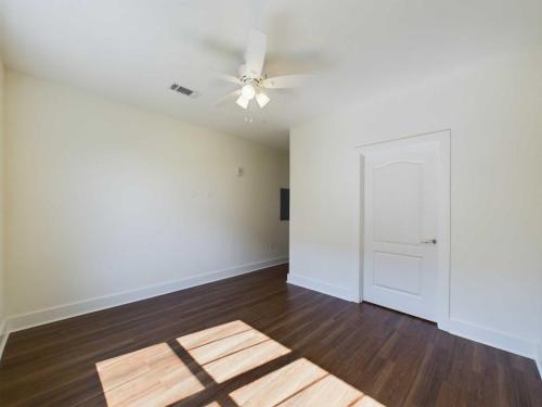 Apartments in Lebanon, IN An empty room with white walls, a ceiling fan, a closed white door, and sunlight streaming through a window onto dark wooden floors.