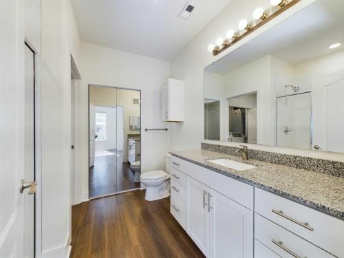 Apartments in Lebanon, IN A modern bathroom with white cabinetry, a granite countertop, a large mirror, a toilet, and a glass shower enclosure. The room has hardwood flooring and bright overhead lighting.