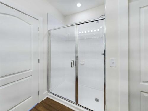 Apartments in Lebanon, IN A modern white shower with sliding glass doors, chrome fixtures, and white tiled walls, located between a door and a light switch on a white wall.