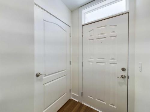 Apartments in Lebanon, IN A white interior door and a white front door with a frosted window panel above it, both with silver handles, in a brightly lit hallway with a wooden floor.