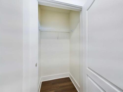 Apartments in Lebanon, IN An empty closet with white walls and a single white wire shelf, featuring brown hardwood flooring and a partially open white door.