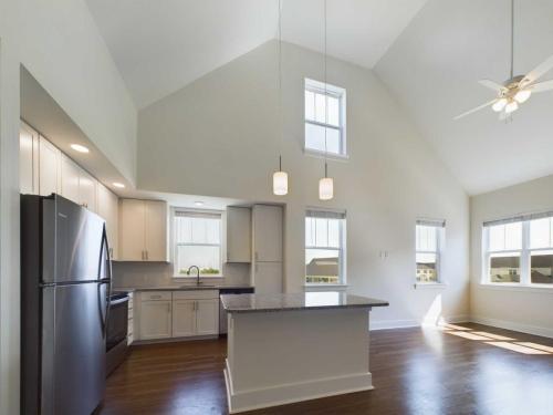 Apartments in Lebanon, IN Spacious, modern kitchen with high ceilings, white cabinets, stainless steel refrigerator, center island, pendant lighting, and hardwood floors, connected to a bright living area with large windows.