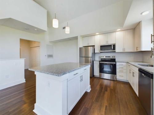 Apartments in Lebanon, IN Modern kitchen with stainless steel appliances, white cabinets, granite countertops, a central island, pendant lights, and hardwood flooring.