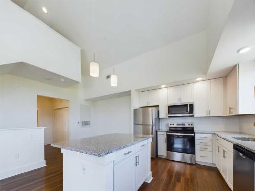 Apartments in Lebanon, IN Modern kitchen with white cabinets, stainless steel appliances, granite countertops, and wooden flooring. Features recessed lighting and hanging pendant lights over an island with built-in storage.