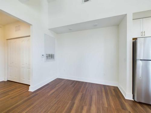 Apartments in Lebanon, IN An empty room with white walls and wooden flooring, featuring a small closet with double doors, an air vent, and a refrigerator partially visible from the right side.