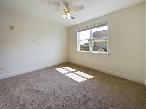 Apartments in Lebanon, IN A bright, empty room with beige carpet, white walls, a ceiling fan, and a window letting in sunlight.