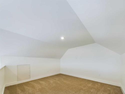 Apartments in Lebanon, IN An empty, white-walled room with a sloped ceiling and a single ceiling light. The floor is covered in brown carpet, and there is a small rectangular door in one wall.