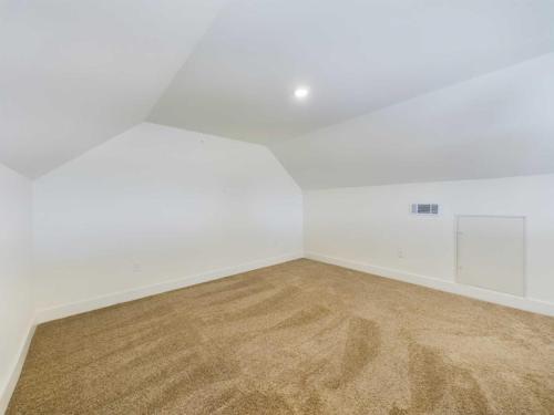 Apartments in Lebanon, IN An empty room with white walls and a pitched ceiling, illuminated by a single light. The floor is carpeted in a light brown color. An air vent and a small door are visible on the right wall.