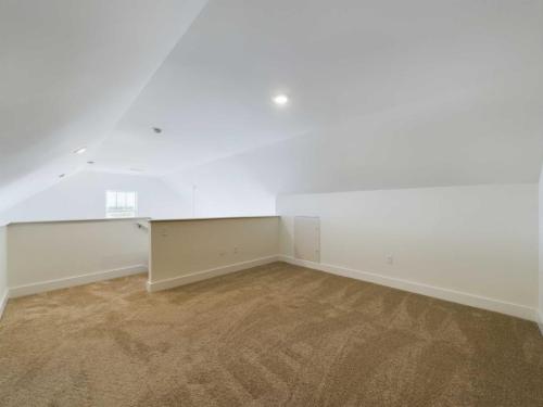 Apartments in Lebanon, IN A spacious loft area with beige carpet, white walls, and a recessed ceiling. The area has a half wall and a small door on the right-hand side. A window is visible at the far end.