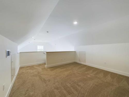 Apartments in Lebanon, IN An empty room with sloped ceilings, beige carpet, white walls, a small door on the side, and a window at the end providing natural light.