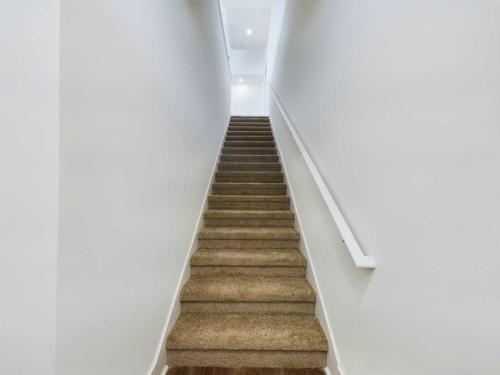 Apartments in Lebanon, IN A carpeted staircase with white walls and a handrail on the right side, leading upwards towards a bright area at the top.