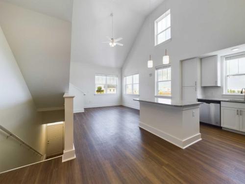 Apartments in Lebanon, IN A spacious, bright living room with high ceilings, large windows, hardwood floors, and a kitchen area with an island. A staircase is visible on the left side.