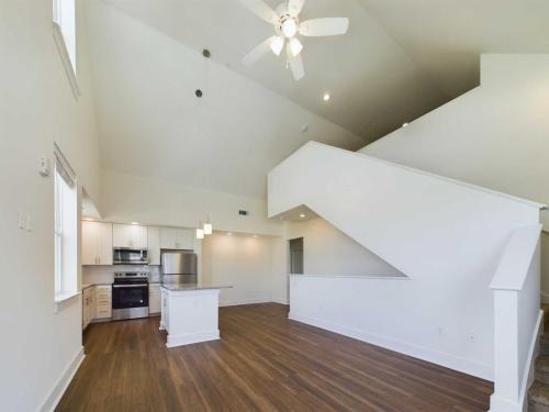 Apartments in Lebanon, IN A modern, unfurnished open-concept living space with a high ceiling, ceiling fan, wooden floors, white walls, and a kitchen with stainless steel appliances. There is a staircase on the right side.