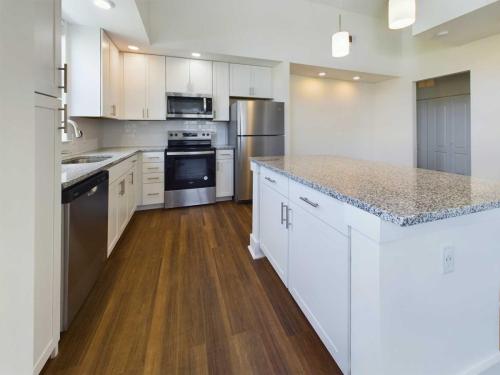 Apartments in Lebanon, IN Modern kitchen with stainless steel appliances, white cabinetry, granite countertops, and wooden flooring. An island with storage and overhead lighting features prominently in the center.