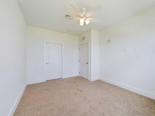 Apartments in Lebanon, IN An empty room with beige carpet, white walls, a ceiling fan with lights, and two white doors.