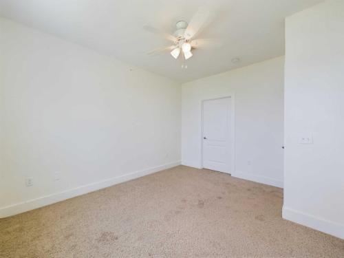 Apartments in Lebanon, IN An empty room with beige carpet, a white ceiling fan, white walls, and a closed white door.