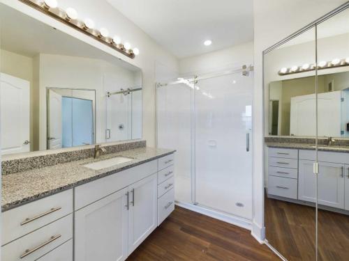 Apartments in Lebanon, IN Modern bathroom with a double-sink vanity featuring granite countertops and ample cabinetry. Includes a glass-enclosed shower and mirrored closet doors, with wood flooring and overhead lighting.