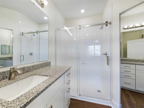 Apartments in Lebanon, IN Modern bathroom with marble countertop sink on the left, large mirror, and a glass-enclosed shower with sliding doors. White cabinetry and wood flooring complete the contemporary design.