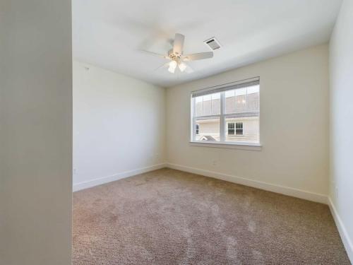 Apartments in Lebanon, IN A carpeted bedroom with a ceiling fan, a window with blinds, and white walls.