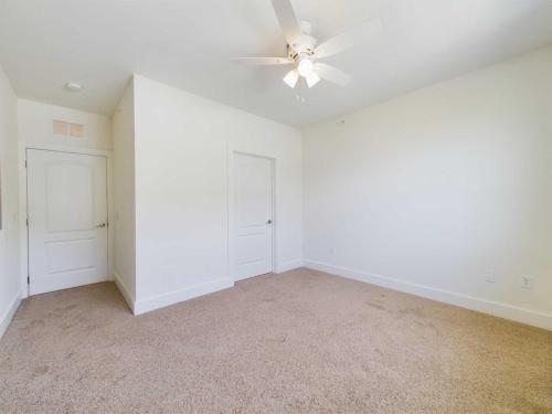 Apartments in Lebanon, IN A bright, empty room with beige carpet, white walls, a ceiling fan, and two closed white doors.