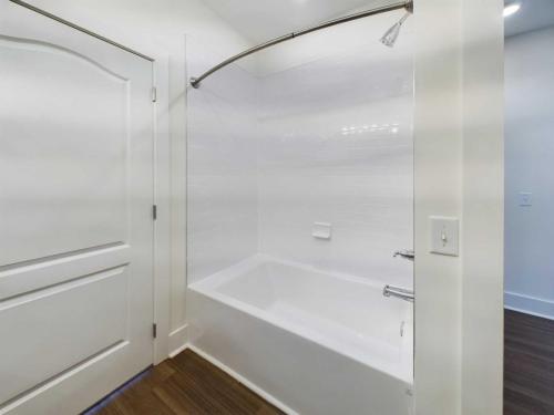 Apartments in Lebanon, IN A bathroom featuring a white bathtub with wall tiles and a curved shower rod above. The floor has wood-style flooring, and there's a white door on the left side.