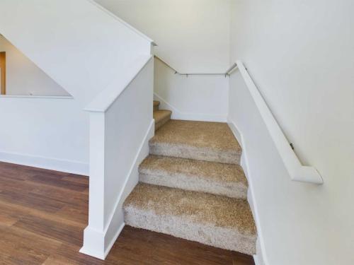 Apartments in Lebanon, IN A carpeted staircase with white railings and white walls, leading to an upper floor. The floor beside the stairs is wooden.