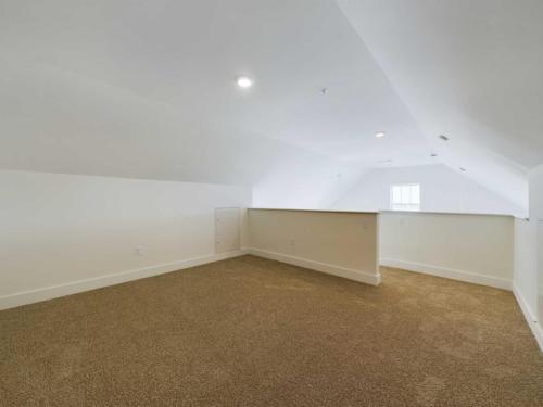 Apartments in Lebanon, IN A spacious attic room with beige carpet, white walls, and a low ceiling. The room is well-lit with recessed lights and has a half-wall separating two areas.