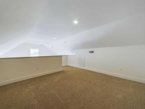 Apartments in Lebanon, IN A spacious, carpeted attic room with white walls and a slanted ceiling, featuring two ceiling lights and a small window in the distance.