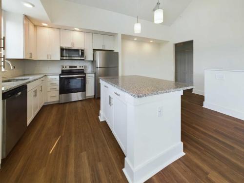 Apartments in Lebanon, IN Modern kitchen with white cabinets, stainless steel appliances, granite countertops, and hardwood floors. The kitchen features a large island with hanging pendant lights and ample workspace.