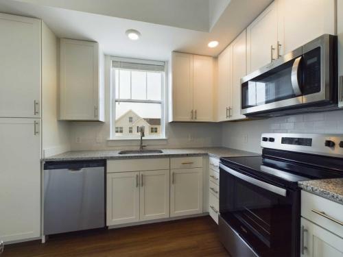 Apartments in Lebanon, IN Modern kitchen with white cabinets, granite countertops, stainless steel appliances including dishwasher, oven, and microwave, and a window above the sink. Wood flooring throughout.