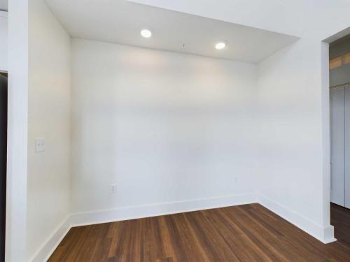 Apartments in Lebanon, IN A white-walled corner of a room with recessed lighting and dark wood flooring. The ceiling extends into a small alcove, and an electrical outlet is visible on the left wall.