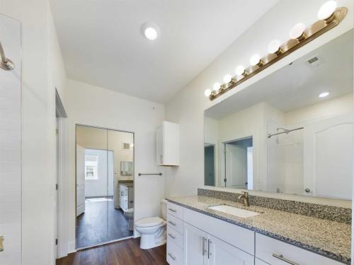 Apartments in Lebanon, IN Modern bathroom with white cabinets, granite countertop, single sink, large mirror, and wood flooring. Includes a toilet and a view into an adjacent space. Bright lighting from fixtures above the mirror.