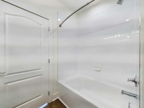 Apartments in Lebanon, IN A clean white bathroom with a bathtub-shower combo, a curved shower rod, white tiles on the wall, and a white door to the left.