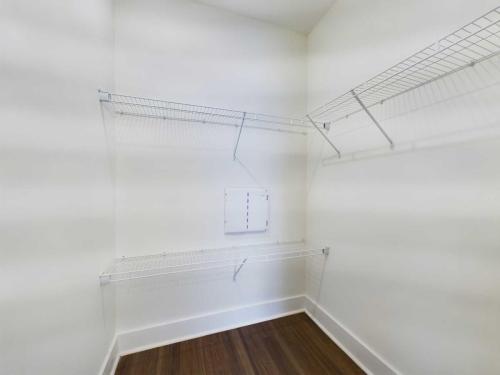 Apartments in Lebanon, IN A small, empty walk-in closet with wooden flooring and white walls, featuring three metal wire shelves on either side.