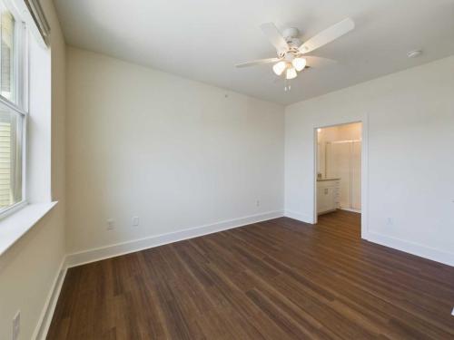 Apartments in Lebanon, IN An empty room with light-colored walls, a ceiling fan with lights, wood flooring, a window on the left wall, and an open doorway leading to a bathroom or another room.